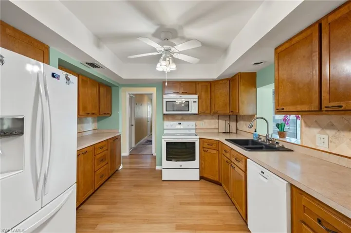 Kitchen with ceiling fan, backsplash, light hardwood / wood-style flooring, and white appliances