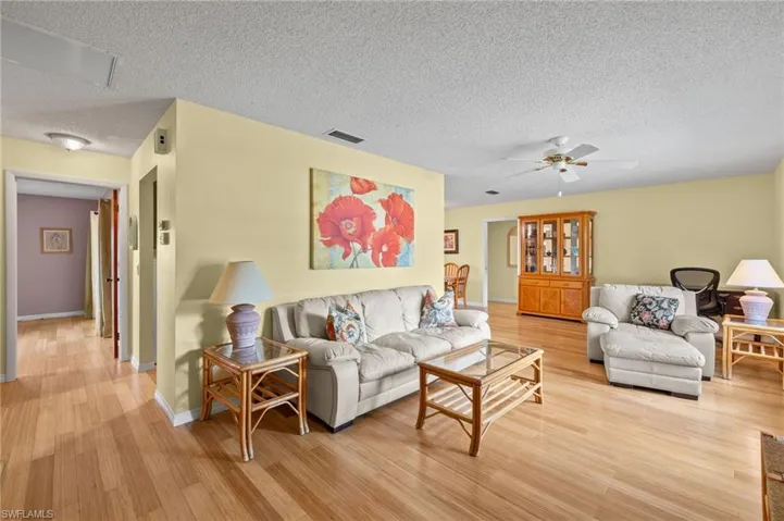 Living room with a textured ceiling, light wood-type flooring, and ceiling fan