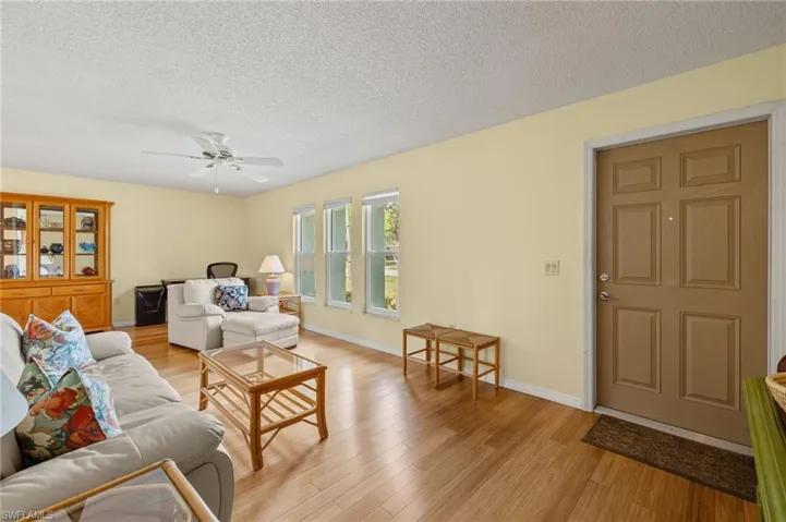 Living room with a textured ceiling, ceiling fan, and light hardwood / wood-style floors