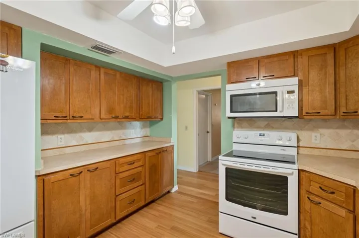 Kitchen featuring ceiling fan, decorative backsplash, white appliances, and light hardwood / wood-style floors