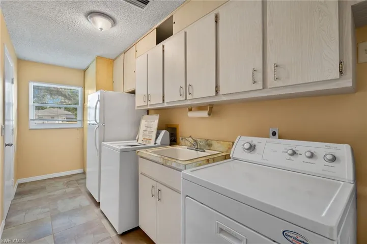 Laundry area featuring washing machine and dryer, sink, a textured ceiling, and light tile patterned flooring