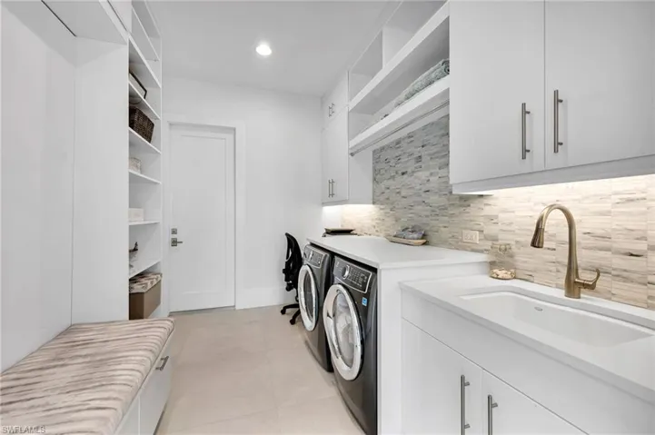 Clothes washing area featuring washing machine and dryer, cabinets, light tile patterned flooring, and sink