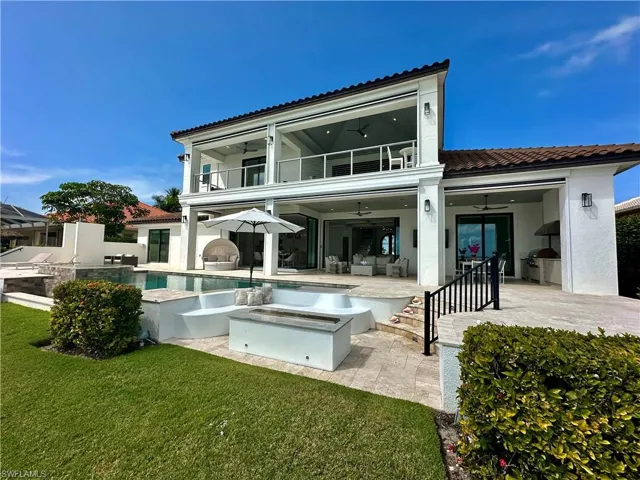 Back of house with exterior kitchen, a balcony, ceiling fan, a swimming pool with hot tub, and a patio