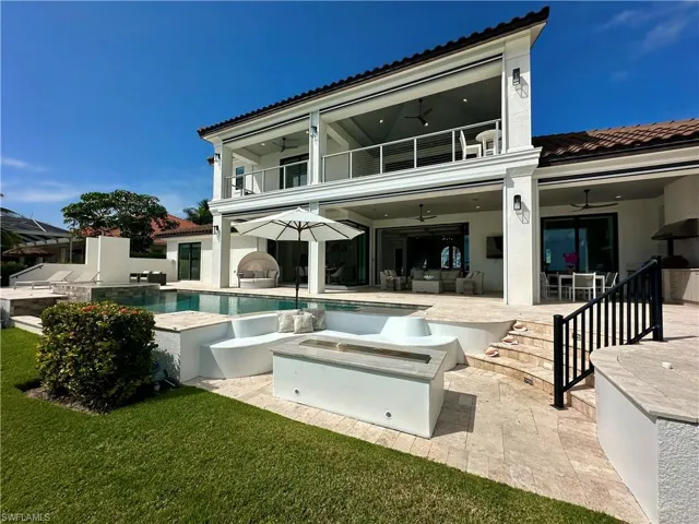 Rear view of house featuring ceiling fan, exterior kitchen, a balcony, and a swimming pool with hot tub