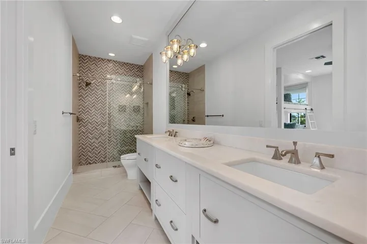 Bathroom featuring tile patterned floors, vanity, toilet, a chandelier, and a tile shower