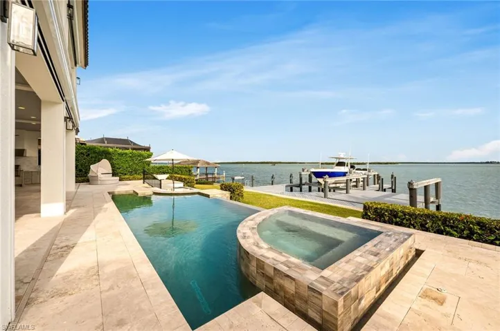 View of pool with a water view, a dock, a patio, and an in ground hot tub