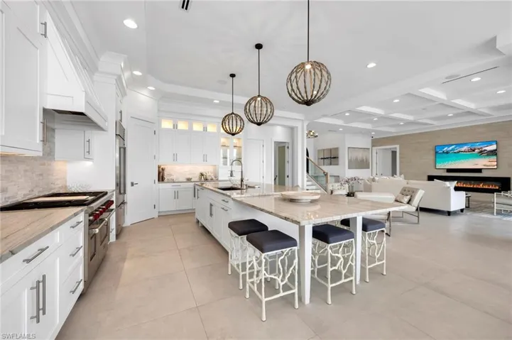 Kitchen featuring beam ceiling, coffered ceiling, high end appliances, a kitchen island with sink, and white cabinets