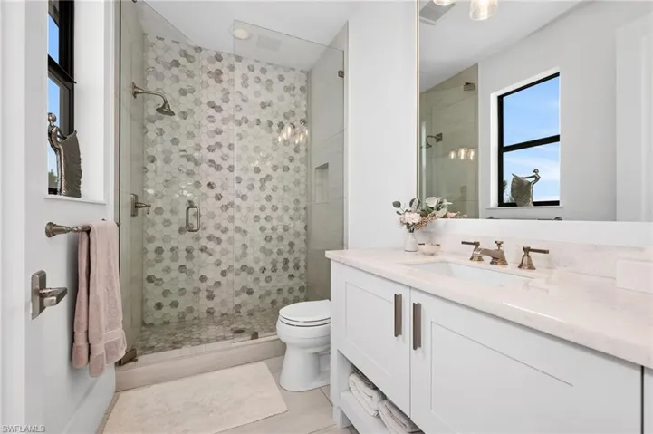 Bathroom with an enclosed shower, vanity, toilet, and tile patterned flooring