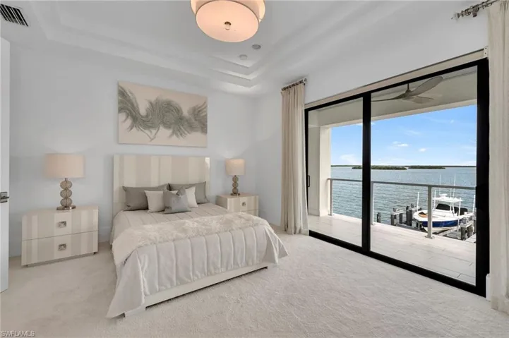 Bedroom with light colored carpet, a water view, a tray ceiling, and access to outside