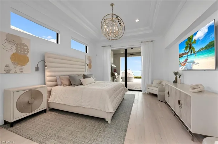 Bedroom featuring access to exterior, multiple windows, a raised ceiling, and a chandelier
