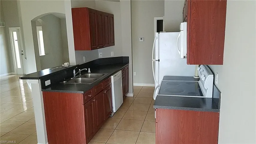 Kitchen with dark countertops, light tile patterned floors, white appliances, and arched walkways