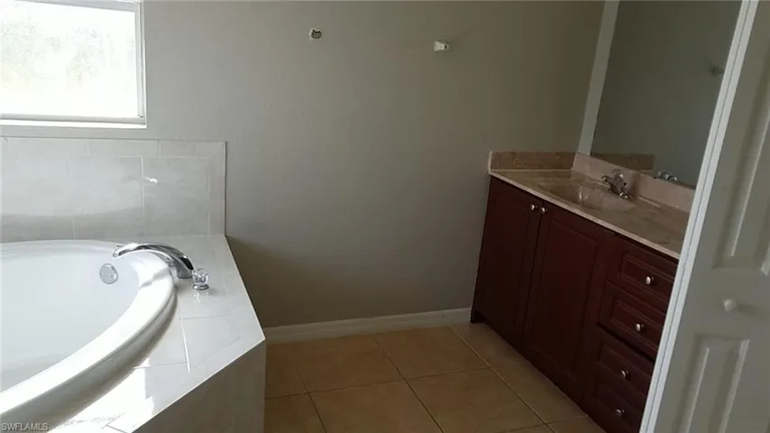 Full bathroom featuring vanity, a garden tub, and light tile patterned floors