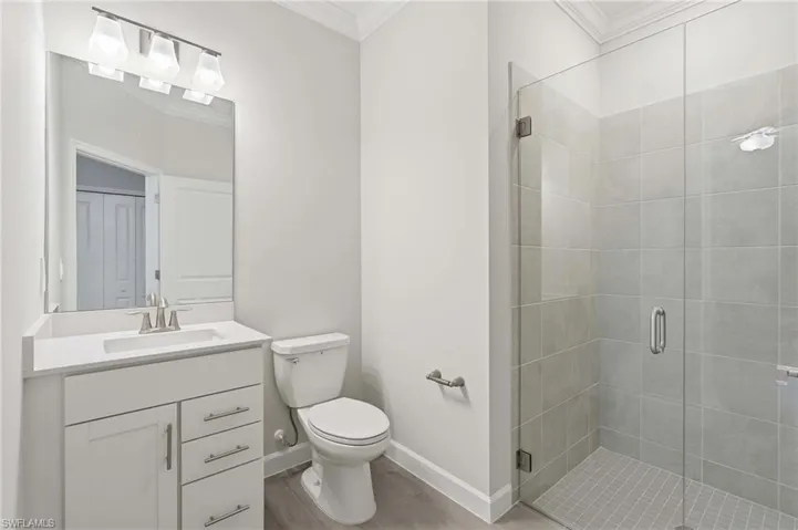 Modern bathroom featuring a glass-enclosed shower with large format tile, a white vanity with a rectangular undermount sink, brushed nickel fixtures, and wood-finish flooring