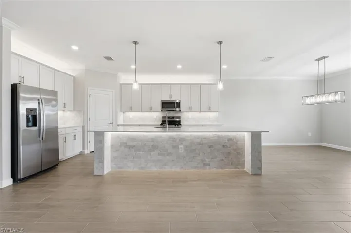 Open-concept kitchen featuring an illuminated island with a stone veneer base, stainless steel appliances, white cabinetry, a light-toned backsplash, and wood-finish flooring
