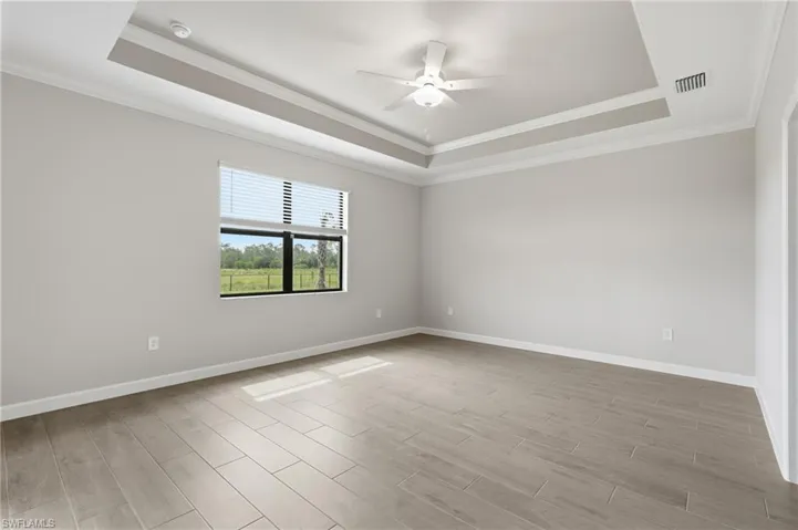 Spacious room featuring a tray ceiling, ceiling fan with integrated lighting, a large window with horizontal blinds, wood-finish flooring, and crown molding