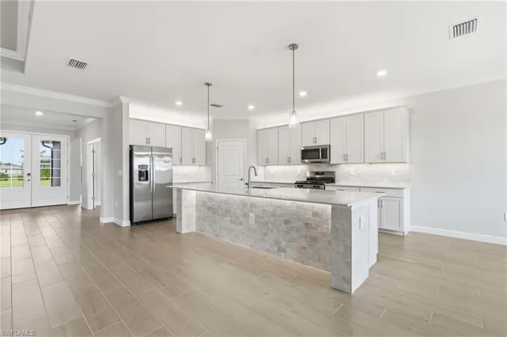 Open-concept kitchen featuring light-toned cabinetry, stainless steel appliances, a large island with stone veneer, pendant lighting, and wood-finish flooring