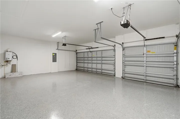 Spacious two-car garage featuring a speckled epoxy flooring, two overhead garage door openers, bright overhead lighting, and a wall-mounted water heater