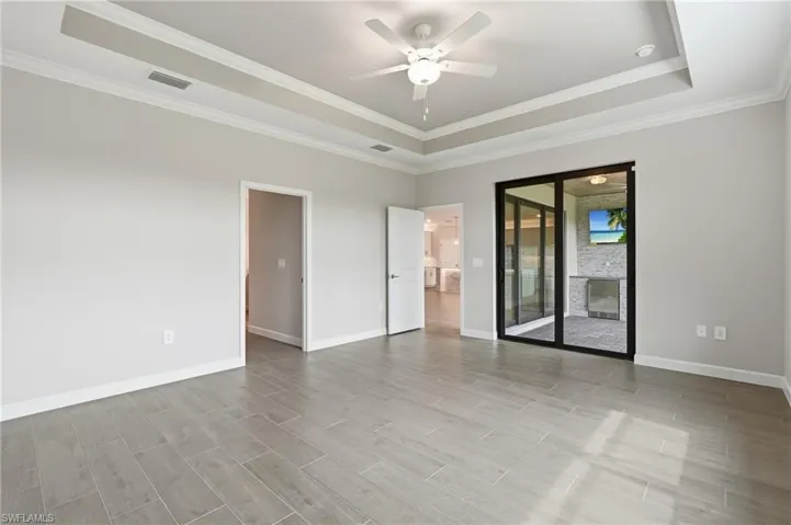 Spacious interior room featuring light wood-finish flooring, a tray ceiling with crown molding, and a ceiling fan