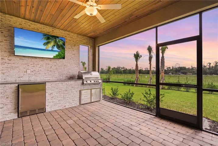 Screened lanai featuring a built-in outdoor kitchen with stainless steel grill and refrigeration unit