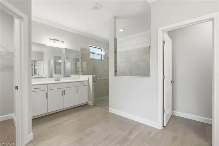 Bathroom featuring a dual vanity with white cabinetry, a walk-in shower with glass enclosure, light-toned tile flooring, and a transom window