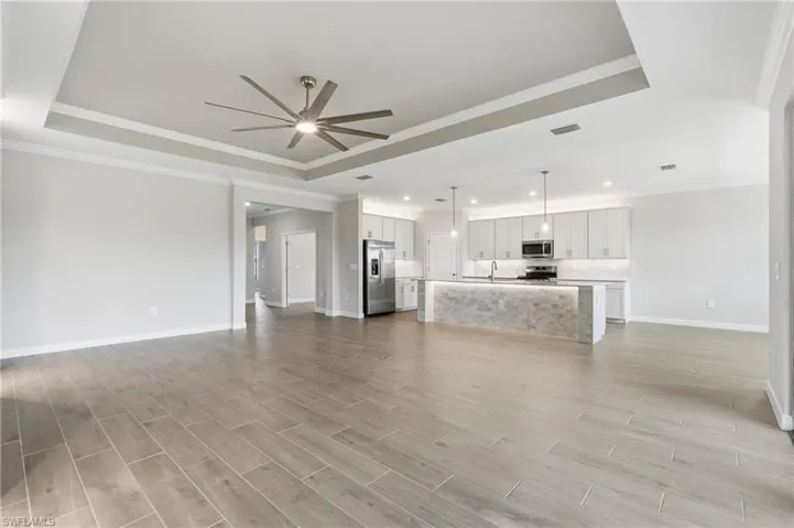 Expansive open-concept living area featuring wood-finish flooring, a tray ceiling with a contemporary ceiling fan, and recessed lighting