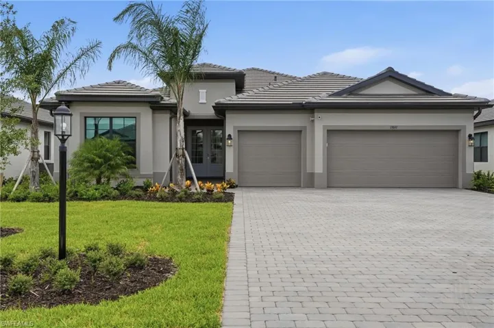 Contemporary stucco exterior with a tile roof, paver driveway, and a two-car garage