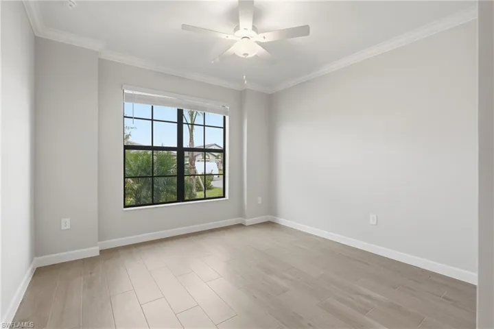 Spacious room featuring a large window with black gridded panes, wood-finish flooring, a ceiling fan, crown molding, and baseboards