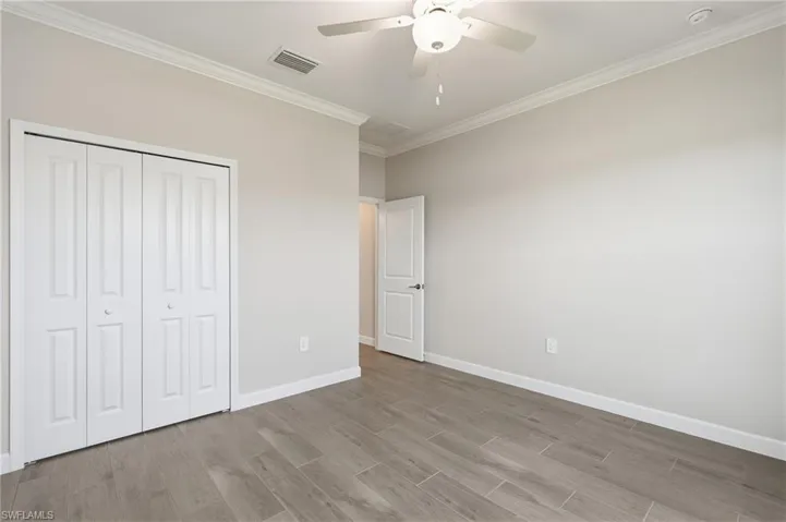 Spacious room featuring wood-finish flooring, light-toned walls, crown molding, and a ceiling fan with integrated lighting