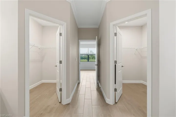 Hallway featuring parallel entryways with wire shelving systems, wood-finish tile flooring, and white trim molding