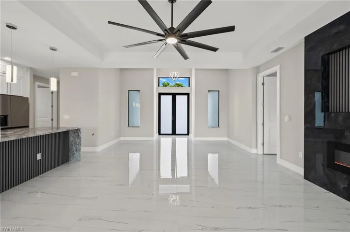 Living room with ceiling fan, a raised ceiling, a large fireplace, and light tile patterned floors