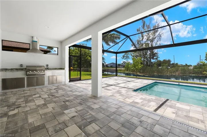 View of swimming pool with an outdoor kitchen, a patio, area for grilling, a lanai, and a water view