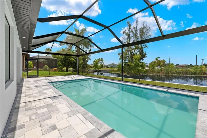 View of swimming pool featuring glass enclosure, a patio, and a water view