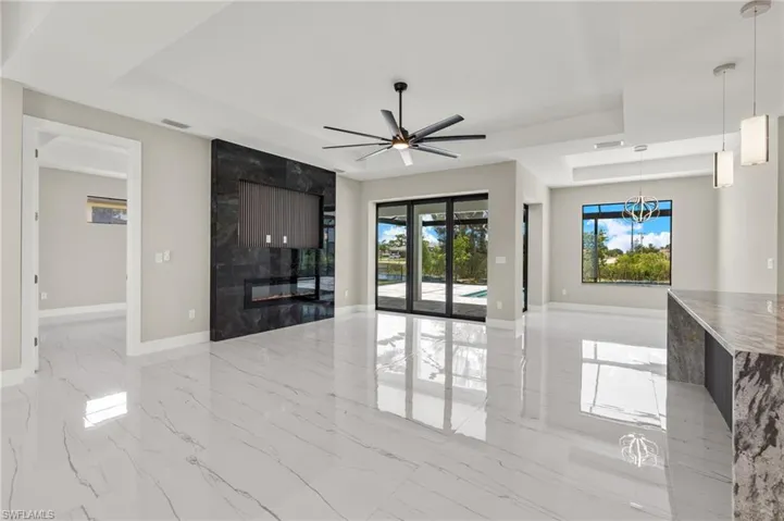 Tiled living room with ceiling fan with notable chandelier, a high end fireplace, and a raised ceiling