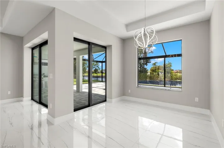Empty room featuring a notable chandelier, light tile patterned flooring, and a tray ceiling