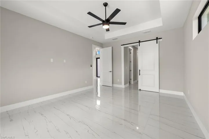 Tiled empty room with ceiling fan, a barn door, and a tray ceiling