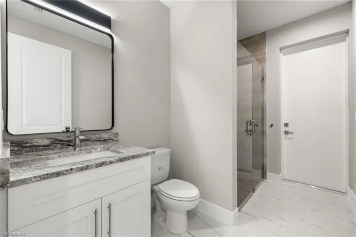 Bathroom with a shower with shower door, vanity, tile patterned floors, and toilet