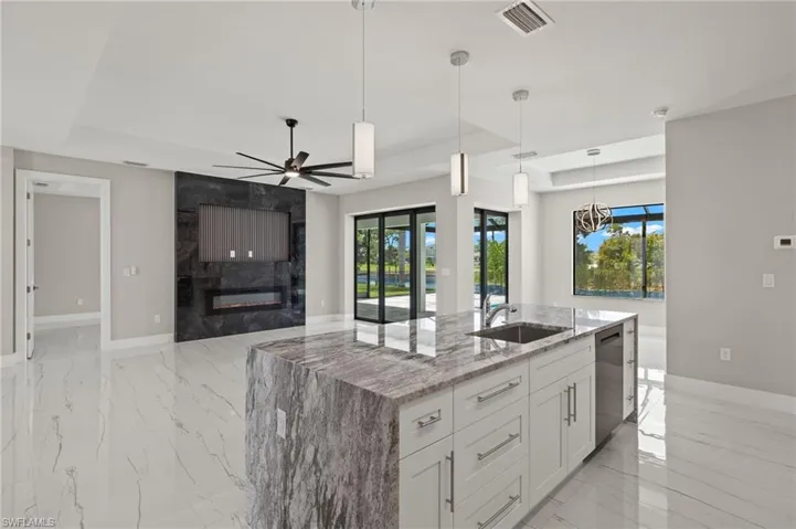Kitchen with a large fireplace, ceiling fan, white cabinetry, stainless steel dishwasher, and sink