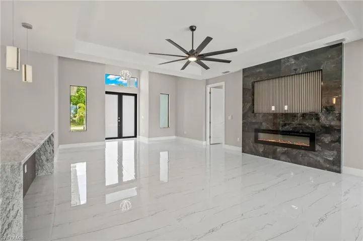 Living room featuring a fireplace, light tile patterned floors, ceiling fan, and a raised ceiling