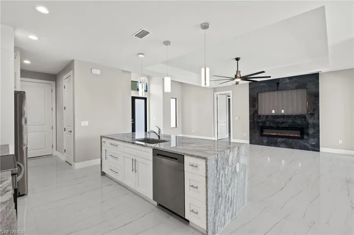 Kitchen featuring appliances with stainless steel finishes, light stone countertops, white cabinets, ceiling fan, and a tiled fireplace
