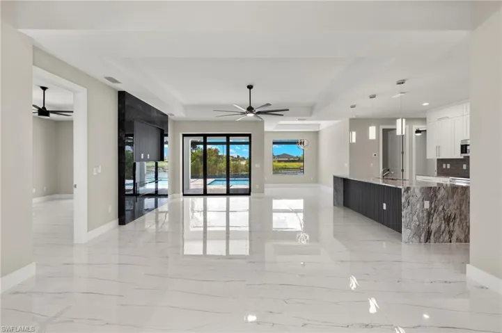 Unfurnished living room featuring ceiling fan, sink, a raised ceiling, and light tile patterned floors