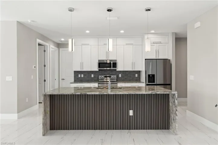 Kitchen featuring light tile patterned flooring, white cabinets, an island with sink, and stainless steel appliances