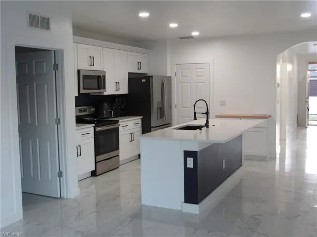 Kitchen featuring arched walkways, stainless steel appliances, white cabinetry, a kitchen island with sink, and recessed lighting