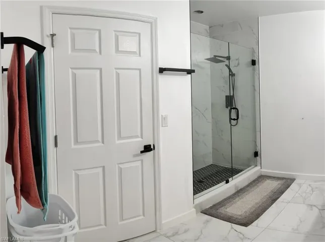 Bathroom featuring light marble finish flooring and a marble finish shower
