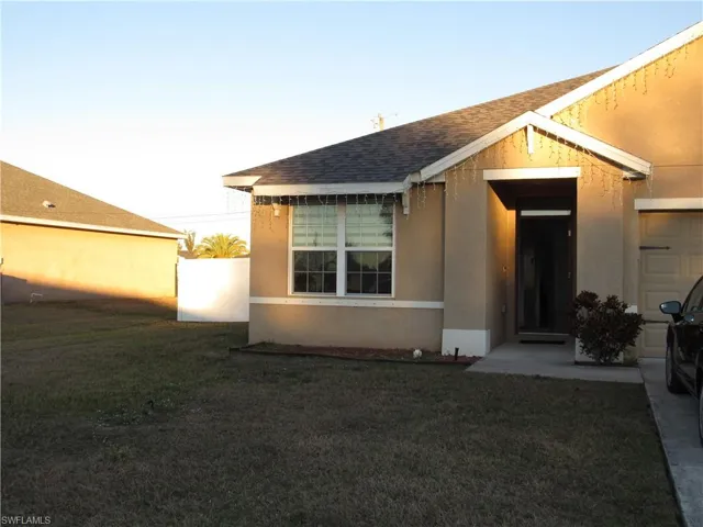 Entrance to property featuring stucco siding, a yard, and a shingled roof