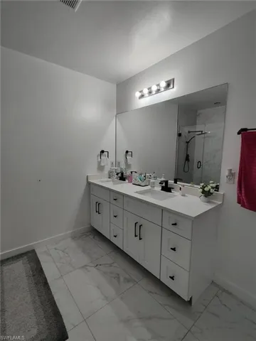 Full bathroom featuring double vanity, a marble finish shower, and light marble finish flooring