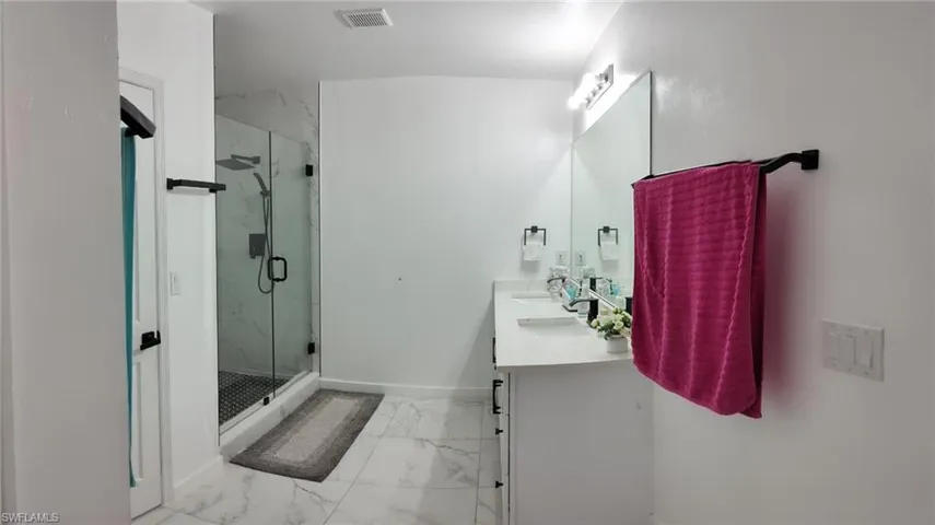 Bathroom with double vanity, a marble finish shower, and light marble finish floors