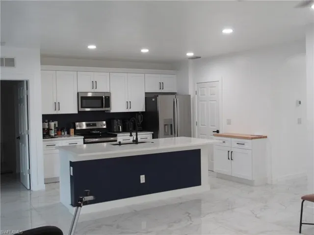 Kitchen featuring white cabinetry, stainless steel appliances, recessed lighting, a center island with sink, and light stone counters