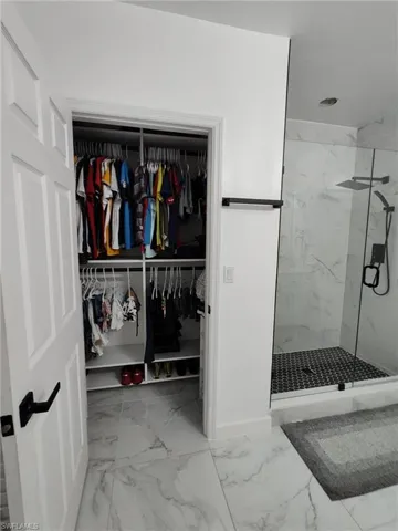 Bathroom with light marble finish flooring, a marble finish shower, and a spacious closet