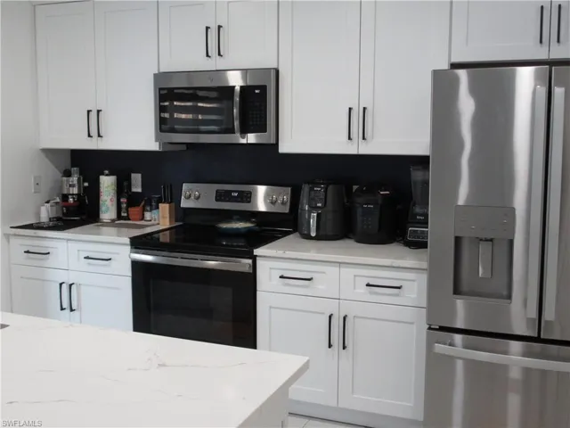 Kitchen featuring appliances with stainless steel finishes, white cabinets, and light stone counters