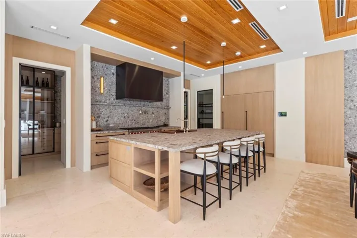 Kitchen with a raised ceiling, light brown cabinets, wooden ceiling, light stone counters, and a kitchen breakfast bar